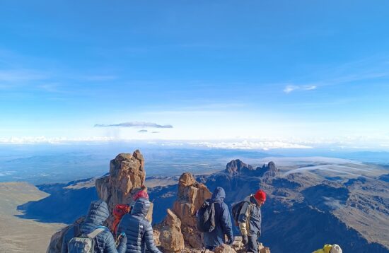 Hikers trekking along the scenic trail amidst lush vegetation with Mount Kenya in the background