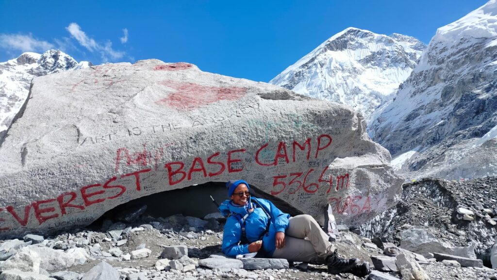 Jane Gatonye standing triumphantly at the base camp of Mt. Everest, surrounded by the breathtaking Himalayan landscape