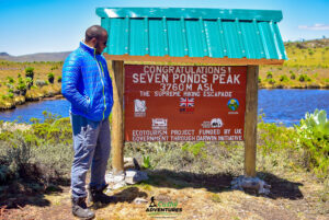 Cushy community hiker posing beside the Seven Ponds summit board