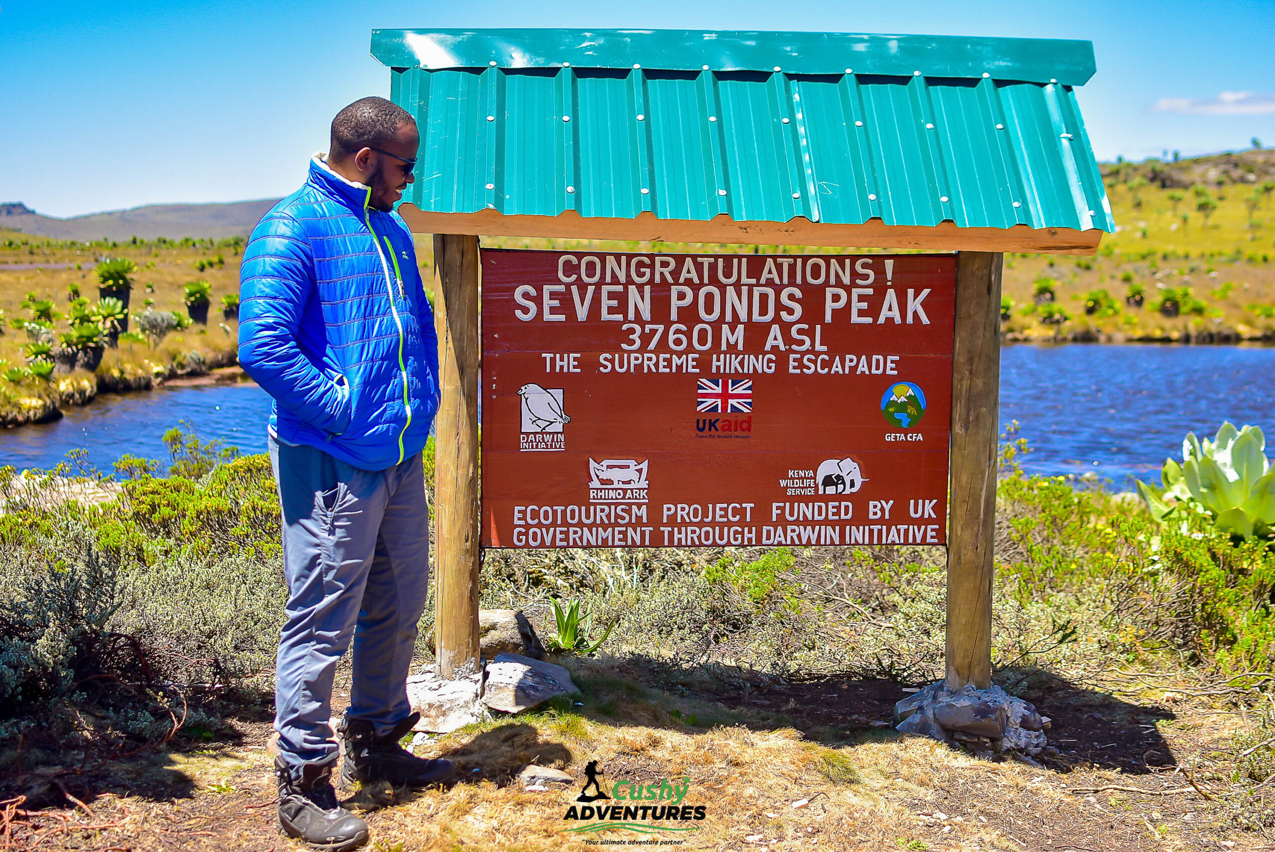 Cushy community hiker posing beside the Seven Ponds summit board