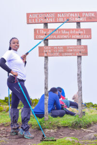 Hiker standing beside Elephant Hill summit board in Aberdares