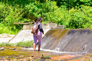 Lady walking barefoot along a stream beside a small reservoir in Namanga Hills forest, providing water to local residents