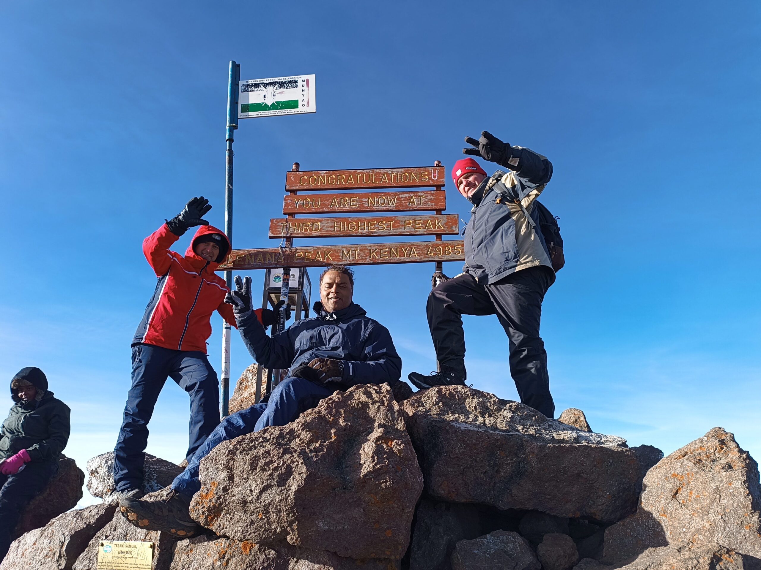 Group of three hikers posing together at the summit of Mount Kenya with scenic views in the background